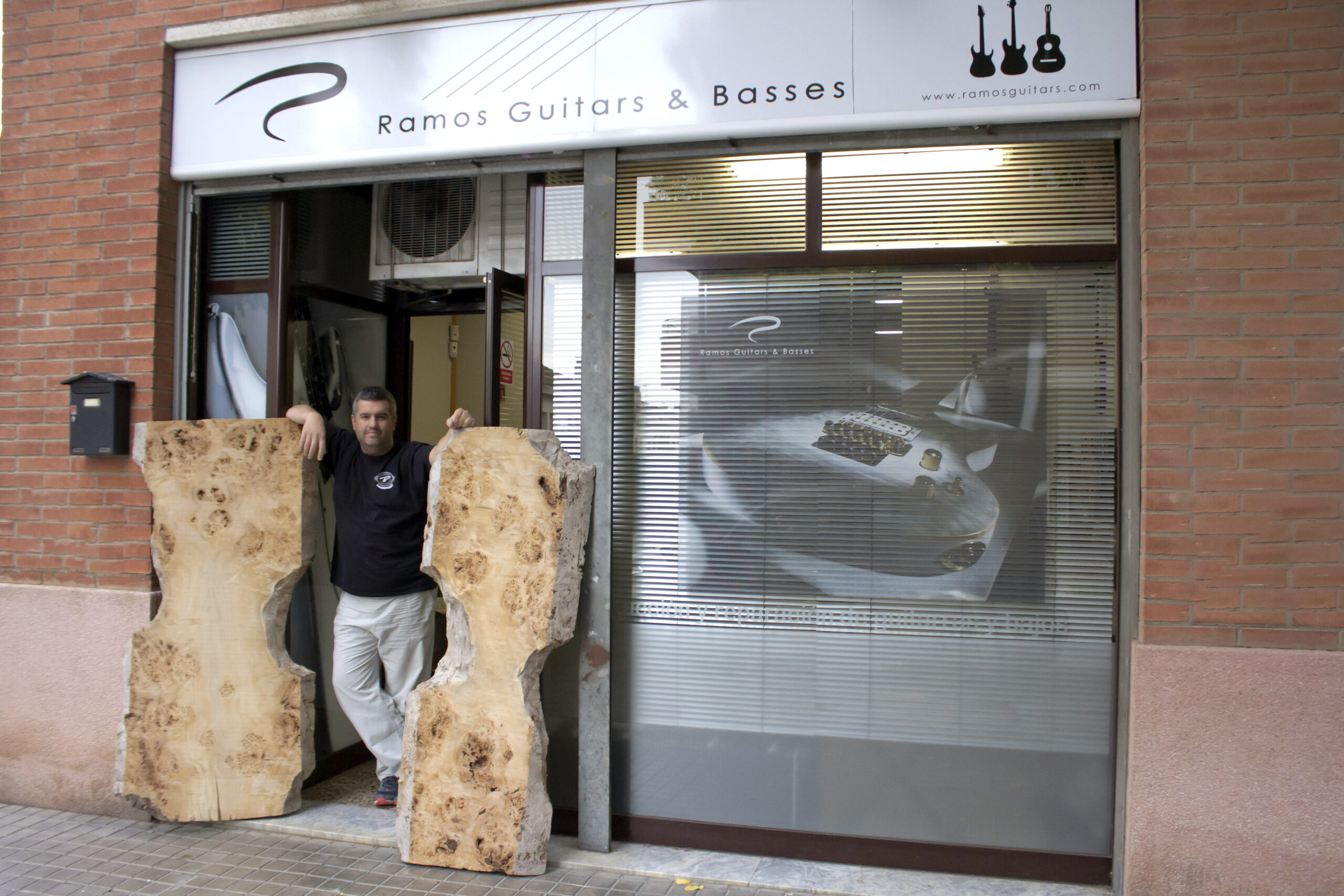 Jose Ramos, master luthier of Ramos Custom Guitars, holding premium wood blanks outside the workshop.